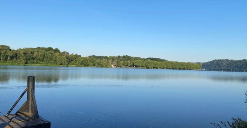 Blick auf den See in Heisingen mit grünem Ufer und klarem Himmel – Sinnbild für Natur und Klimaschutz.